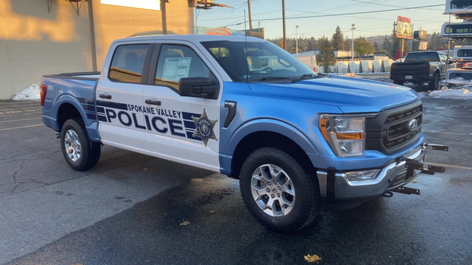 Spokane Valley Police Department's blue and white Ford F-250 patrol truck parked outside, with the police badge and emergency contact number prominently displayed.