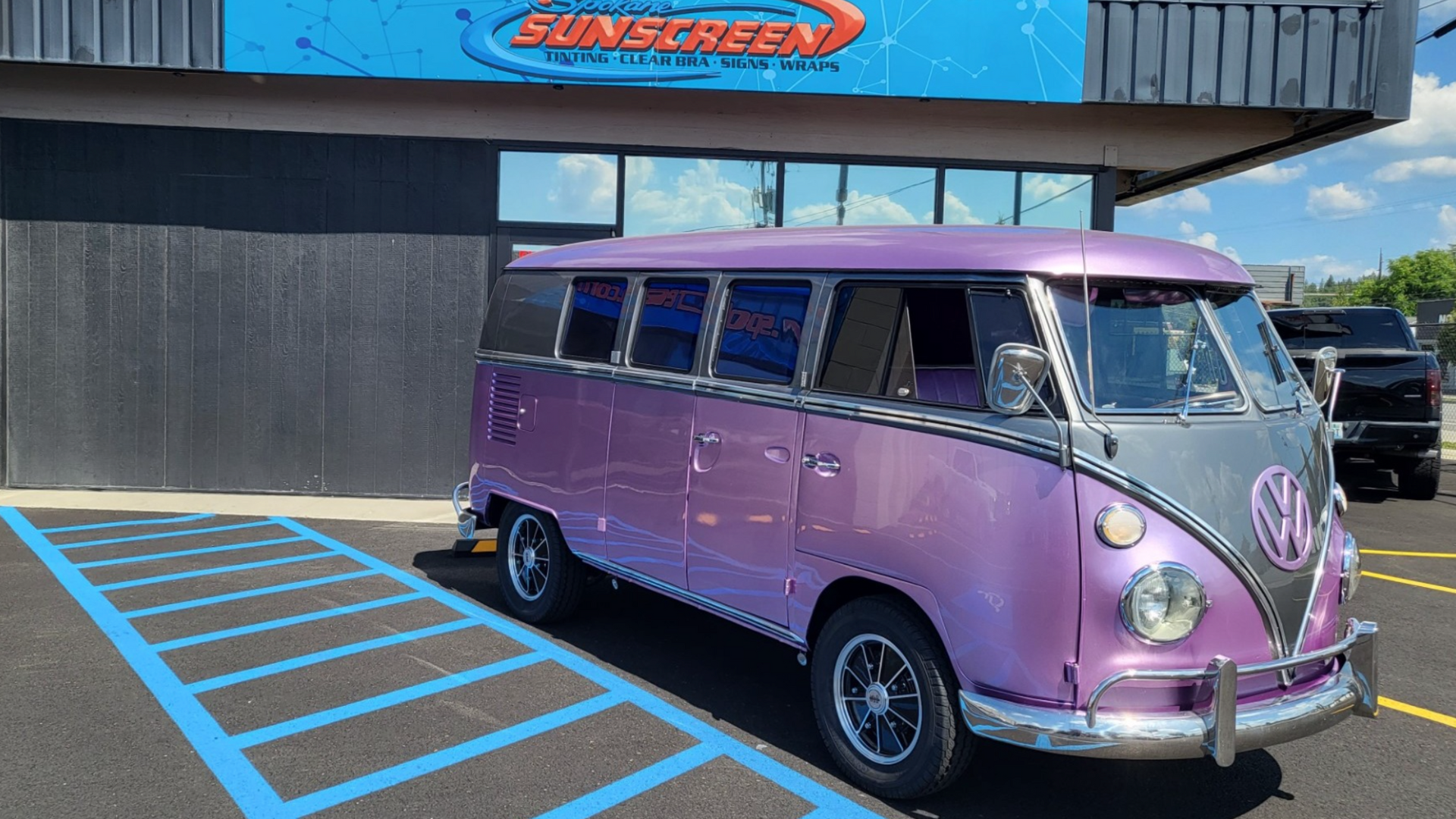 Vintage purple and white Volkswagen bus parked outside Spokane Sunscreen with clear blue skies overhead.