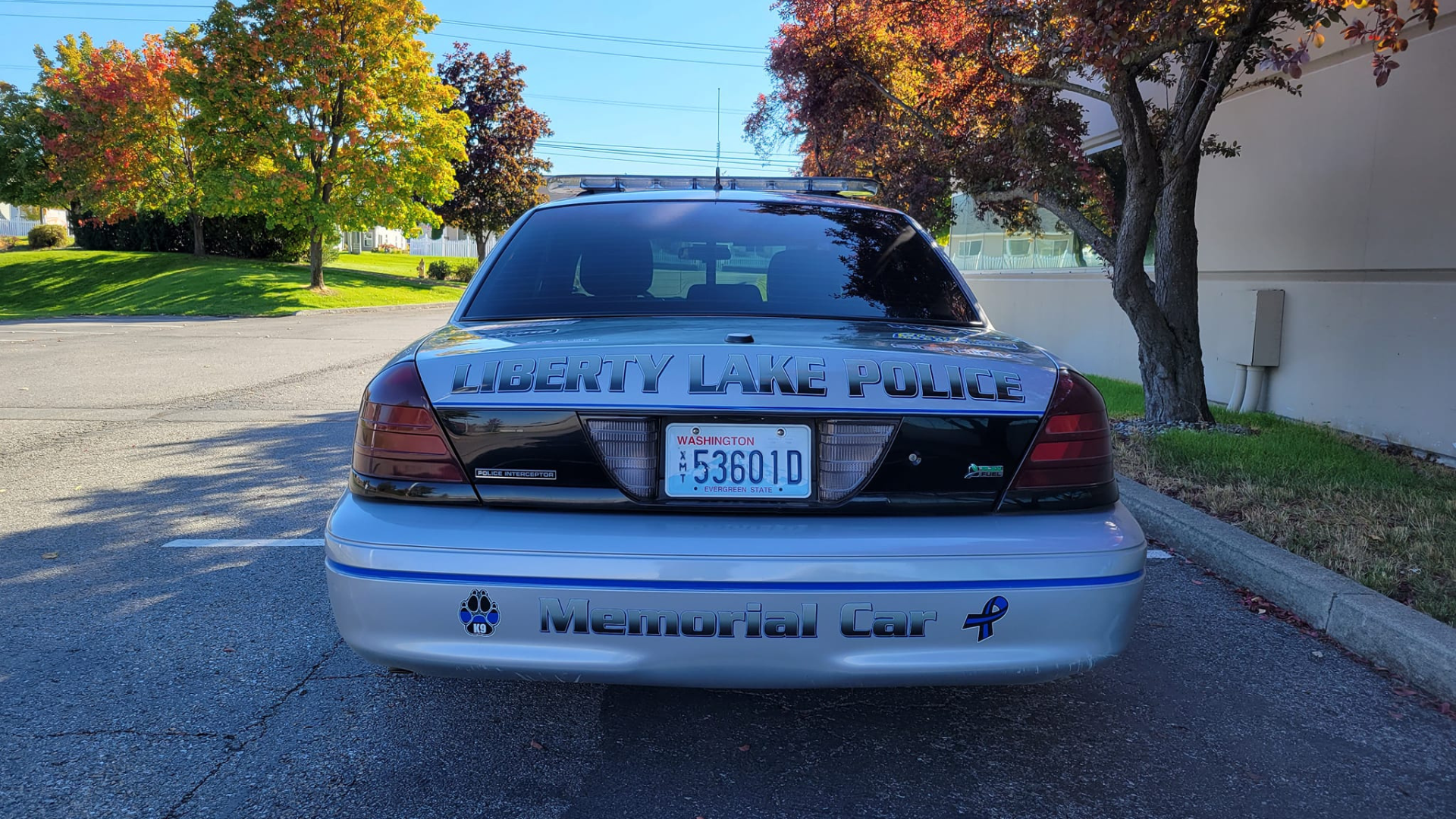 Rear angle of a Liberty Lake Police Memorial Car, showcasing the police logo and the "Memorial Car" label, parked on a suburban street.