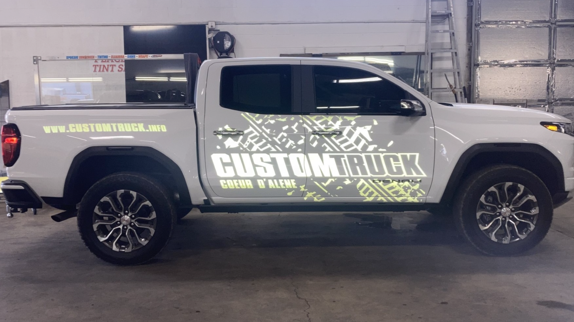 Custom graphics on a white pickup truck advertising 'Custom Truck' in bold, neon-style lettering for Coeur d'Alene dealership.