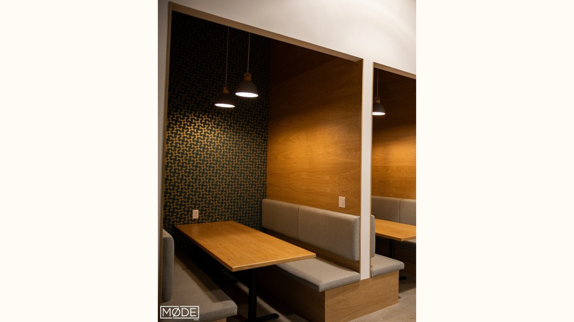 Intimate dining or meeting area in a coworking space with modern design, featuring wooden tables, gray bench seating, and decorative pendant lights above.