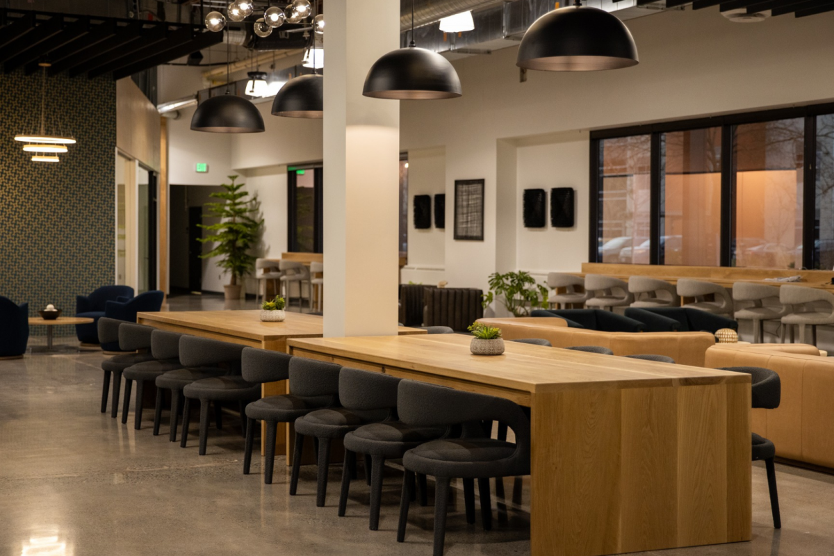 Spacious and well-lit coworking area featuring stylish blue armchairs, wooden tables, and contemporary decor under pendant lighting